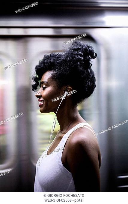 Profile of smiling woman with earphones on subway station platform