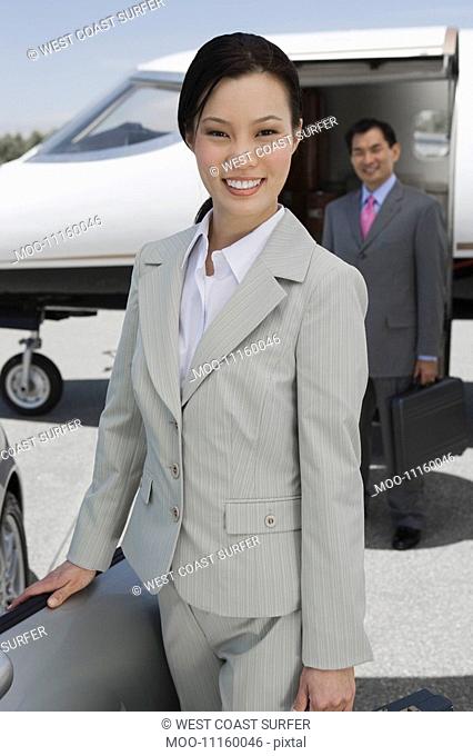 Portrait of mid-adult businesswoman standing in front of convertible mid-adult businessman in background