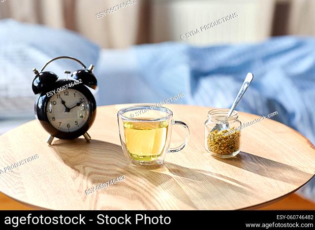 alarm clock and cup of chamomile tea on table