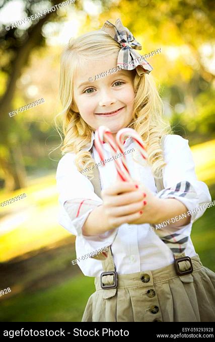 Cute Little Girl with a Bow in Her Hair Holding Her Christmas Candy Canes Outdoors.
