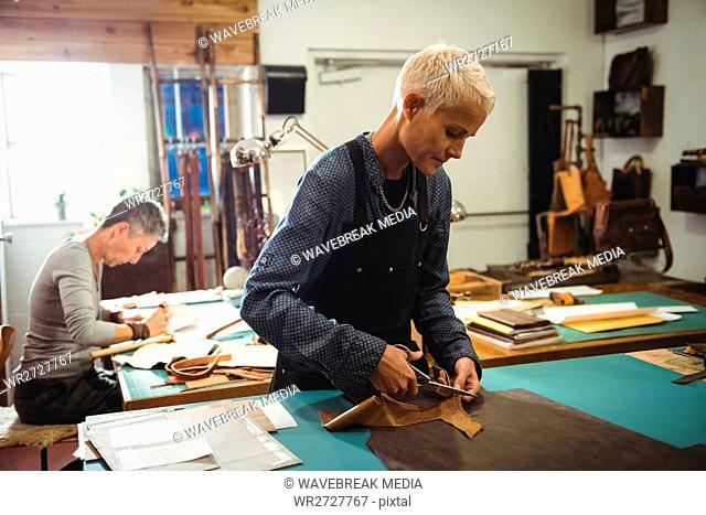 Attentive craftswoman cutting leather