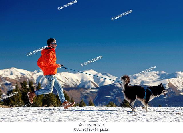 Man running with dog in snow covered mountain landscape