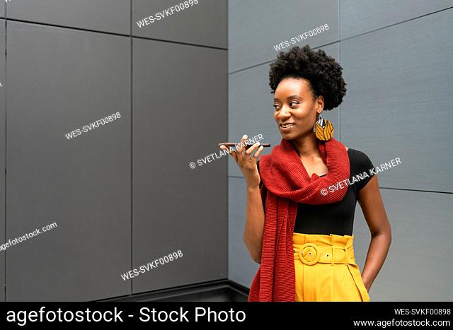 Smiling woman talking on speaker phone in front of gray wall