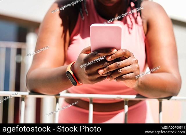Young woman using mobile phone while leaning on railing