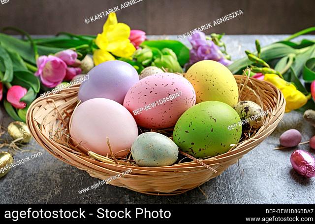 Colorful flowers and painted Easter eggs on grey, stone background. Copy space