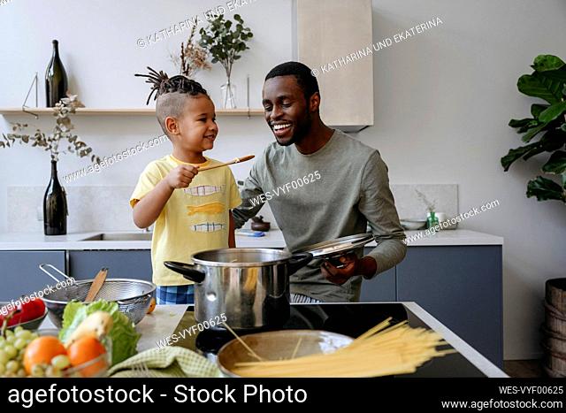 Smiling boy showing spaghetti to father in kitchen