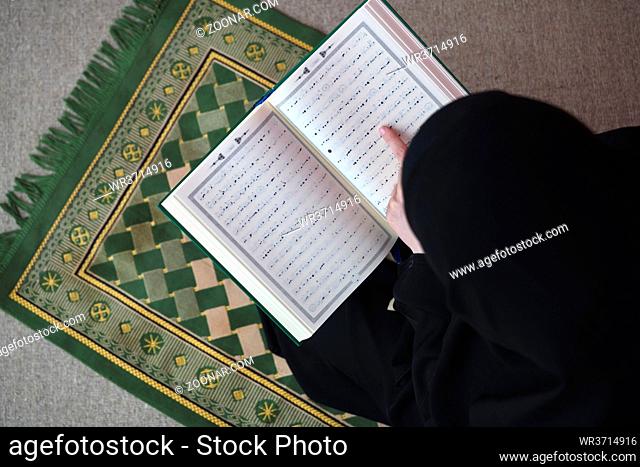 Middle eastern woman praying and reading the holy Quran, public item of all muslims. Education concept of Muslim woman studying The holy Quran at home or mosque...