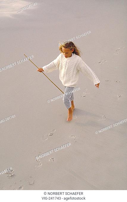 beach-scene, 10-year-old girl wearing white pullover and black-white leggins walks bare feeted with a stick in her hand on the wet sand  - GERMANY, 26/06/2004
