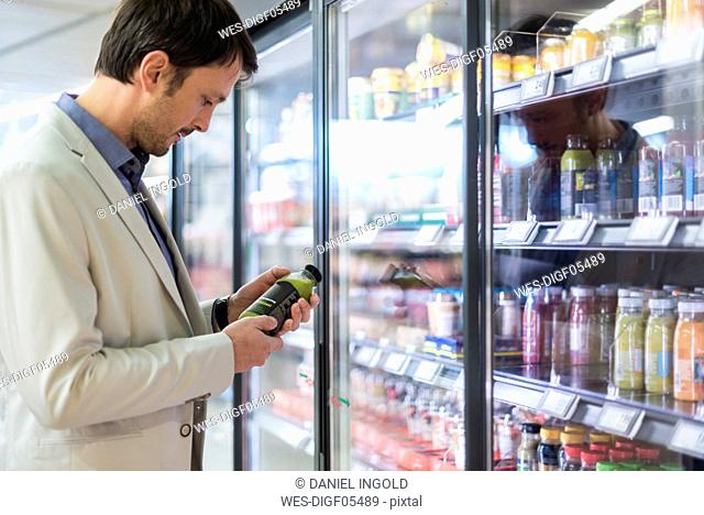 Mature man in supermarket choosing smoothie from cooling shelf
