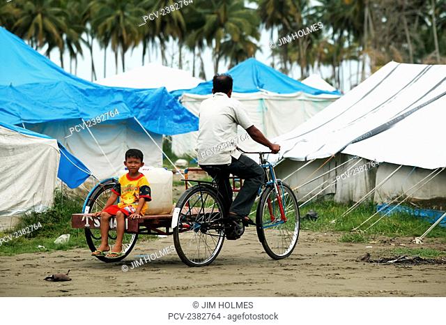 A man and his son cycle back to their home, near Meulaboh, with a large container of water that came from emergency standpipes after the Indian Ocean tsunami in...