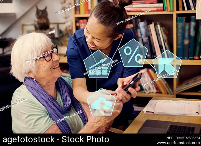 Home carer helping senior woman to use cell phone
