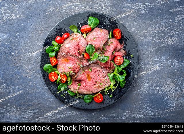 Modern style traditional Commonwealth Sunday roast with sliced cold cuts roast beef served with tomatoes and corn lettuce as top view on a Nordic design plate...