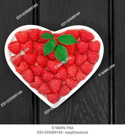 Raspberry fruit in a heart shaped bowl over wooden black background