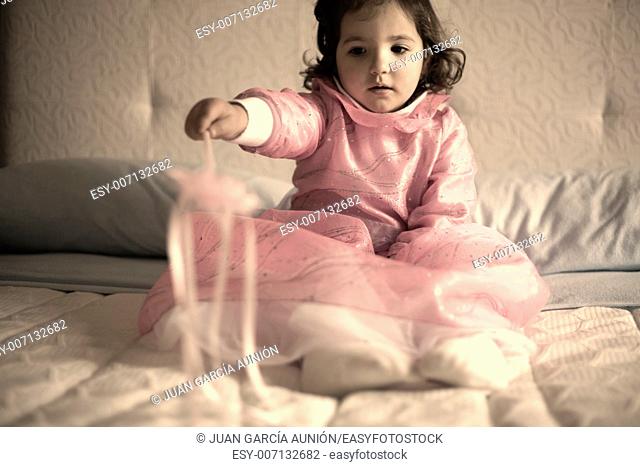 Little girl costumed as a fairy with magic wand sitting on the bed and playing