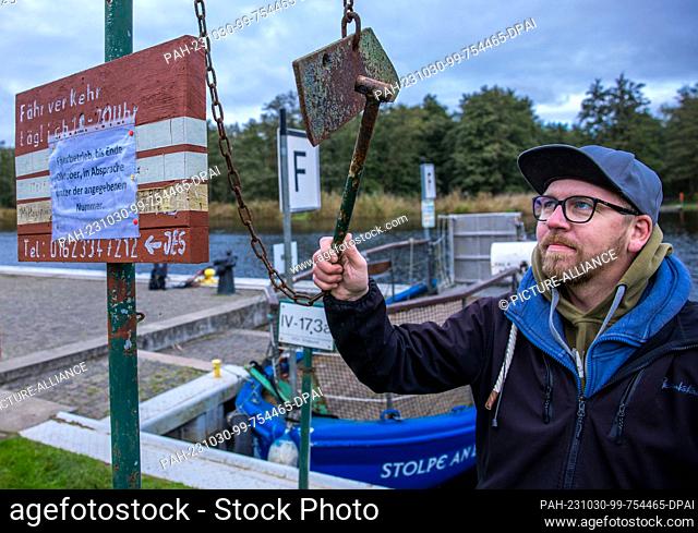 PRODUCTION - 26 October 2023, Mecklenburg-Western Pomerania, Stolpe: A man strikes an iron at the jetty of the small passenger ferry across the Peene and uses...