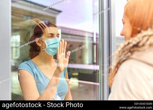 ill woman in mask looking at friend through window