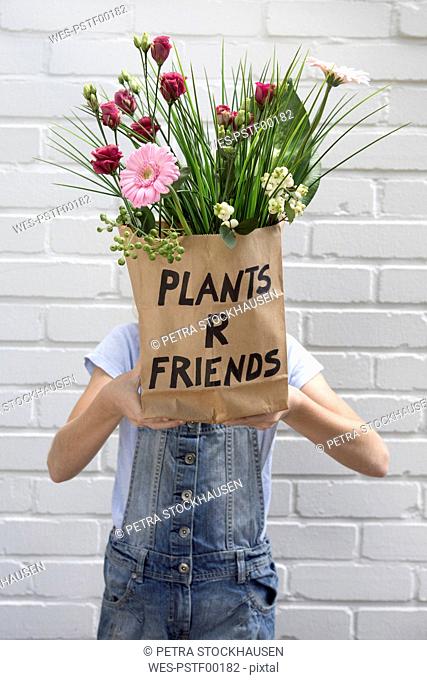 Girl hiding face behind paper bag with flowers