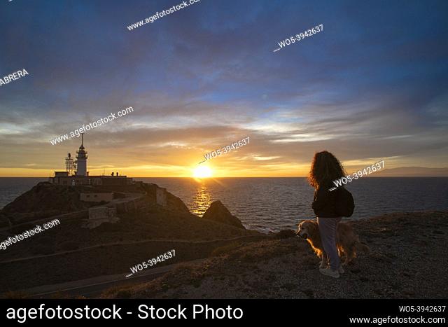 Woman watching sun go down with her dog, in lighthouse of Cabo de Gata, Spain