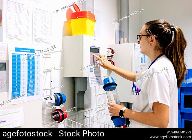 Female doctor using pneumatic tube system while standing in hospital