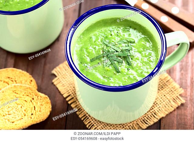 Fresh homemade cream of green pea and mint soup in enamel cups, garnished with stripes of mint leaves (Selective Focus, Focus in the middle of the mint leaves...