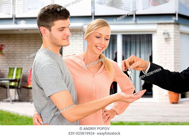 Close-up Of Agent Giving Key Of New Home To Young Happy Couple