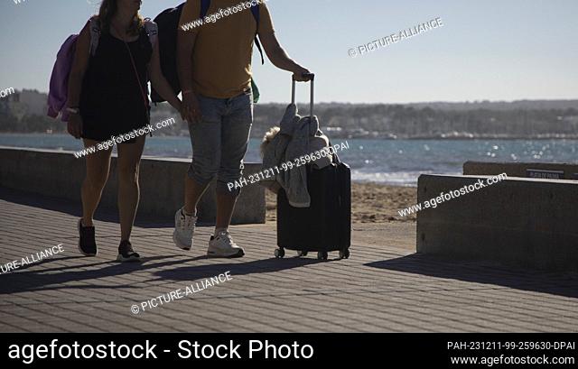 11 December 2023, Spain, Palma: People walk with luggage on the Arenal beach during a sunny day with a record temperature of 24 degrees