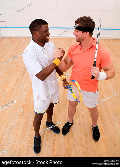 Two men playing match of squash. Handsome men having competition on squash court. Happy smiling and shaking hands