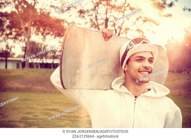 Snowboarding man smiling while holding snowboard in summer flare field. Skiing lifestyle