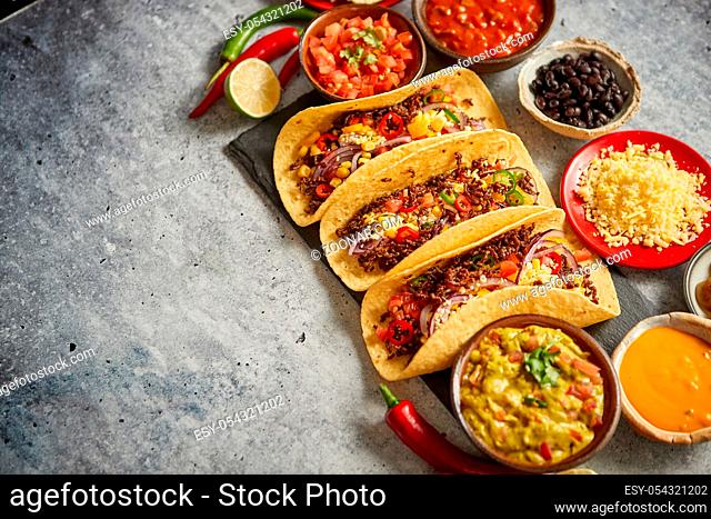 Tasty Mexican meat tacos served with various vegetables and salsa. With sides in ceramic bowls around. Top view composition. Space for text