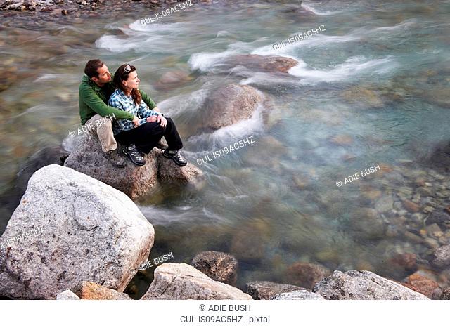 Mid adult couple sitting on rocks in river
