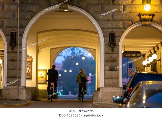Copenhagen, Denmark Bicyclists at night pass an arched passageway and a sign for the local Det Nu Teater theatre in downtown