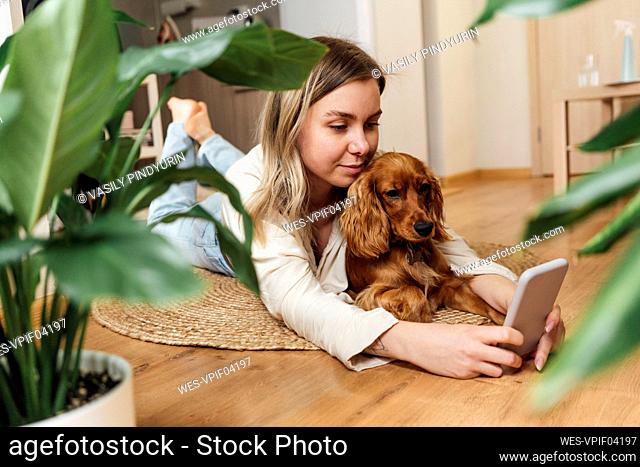 Young woman with Cocker Spaniel using smart phone while lying on floor at home