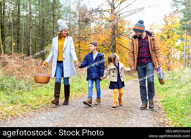 Children holding parents hand while walking on forest path