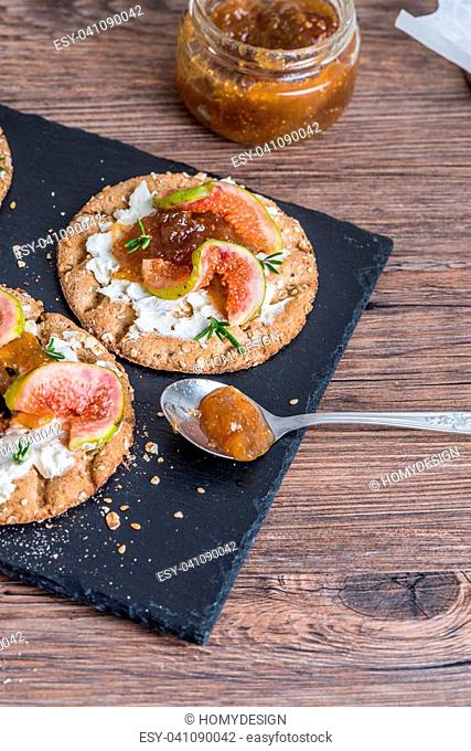 Canape or crostini with multigrain crispread with cream cheese and fig jam on a slate board. Delicious appetizer ideal as an aperitif