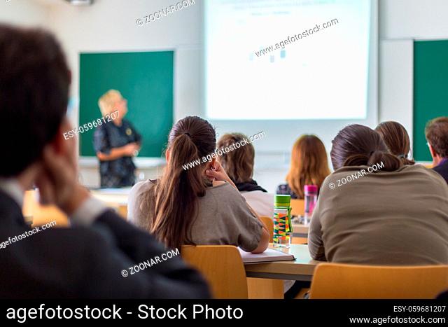 Teacher at university in front of a whiteboard screen. Students listening to lecture and making notes