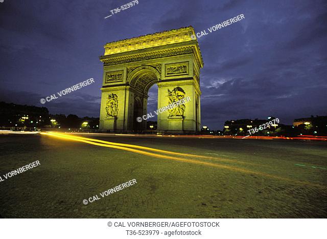 The Arc de Triomphe in Paris is located at the end of the Champs Elysees. This photo shows at night with car headlights as streaks of light. Paris