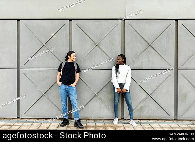 Young man smiling at woman at a grey wall