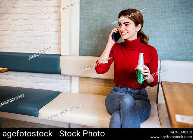 Smiling woman with beer bottle looking away while talking on mobile phone in bar