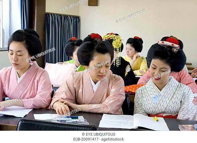 Gion District. Geisha and Maiko apprentice Geisha attending a class at Mia Garatso school of Geisha. Three young women wearing plain kimono seated at desk in...