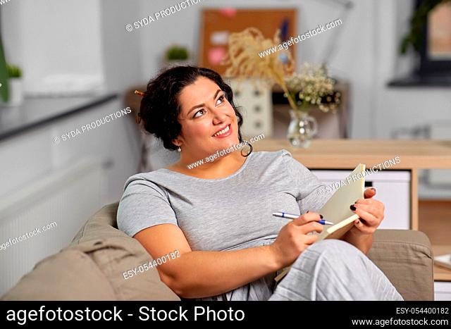 happy young woman with diary on sofa at home