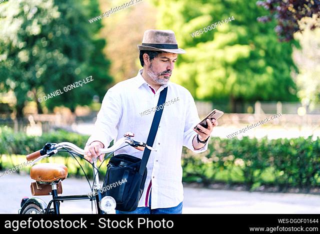 Mature man using mobile phone while standing with bicycle in public park