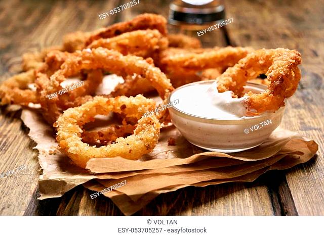 Homemade crunchy fried onion rings with white sauce, close up view