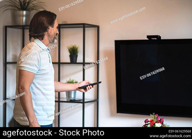TV. Man in a white thsirt spending time at home and switching on tv