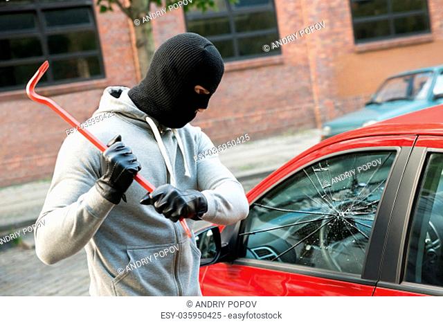 Thief With Mask Trying To Smash The Window Of The Car With Crowbar