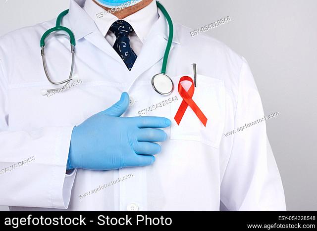 male doctor in a white coat and tie is standing on a white background, red silk ribbon is hanging on his chest, and blue sterile medical gloves are on his hands
