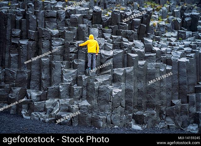 man wearing yellow coat looking up at reynisdrangar basalt columns at reynisfjara beach, iceland
