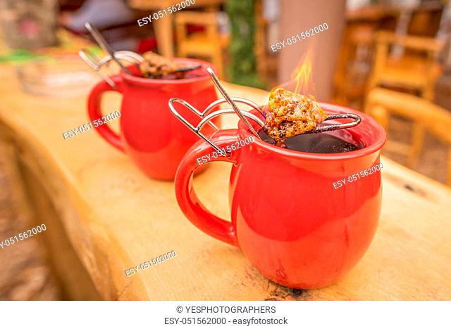 Image with a mug of hot wine, which has tongs with a flaming cone of sugar on top. It is a traditional german drink at Christmas fairs