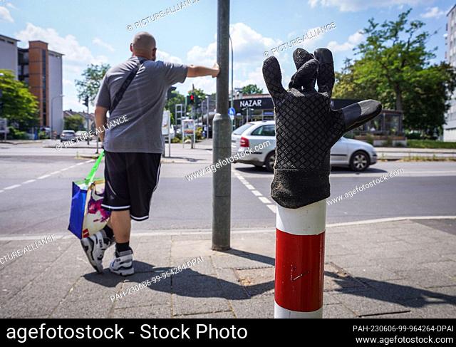 06 June 2023, Hesse, Dietzenbach: A glove, apparently lost in colder weather, slipped over a post on the sidewalk at an intersection in summer afternoon...