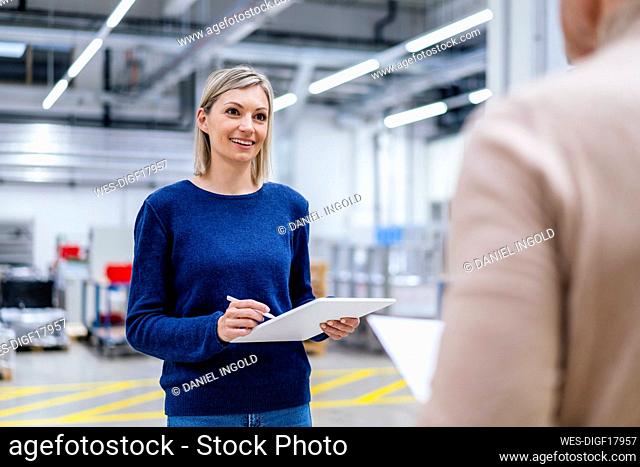 Businesswoman with digital tablet smiling at colleague in factory