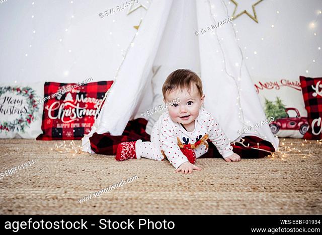 Cute baby girl smiling while crawling against tent during Christmas at home